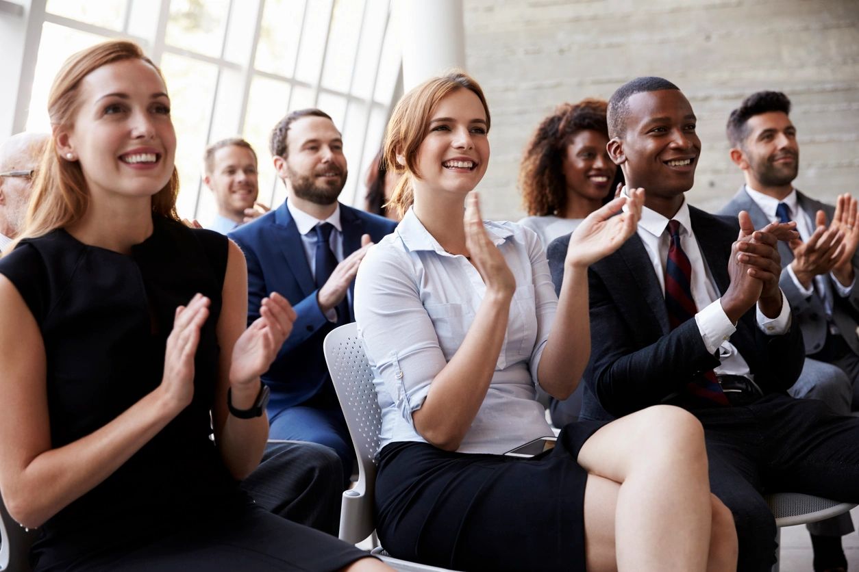 The audience celebrates good news in a business environment, clapping with satisfaction.